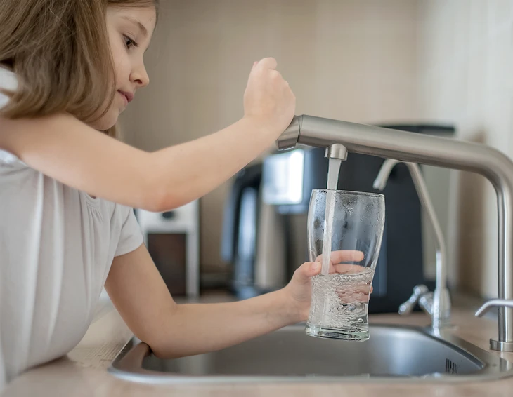 Jeune femme remplit un verre d'eau au robinet de cuisine moderne