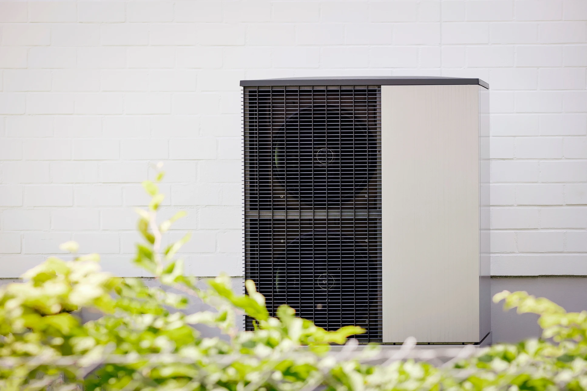 Extérieur résidentiel avec unité de climatisation installée sur lit de gravier décoratif, bordée de pelouse synthétique verte