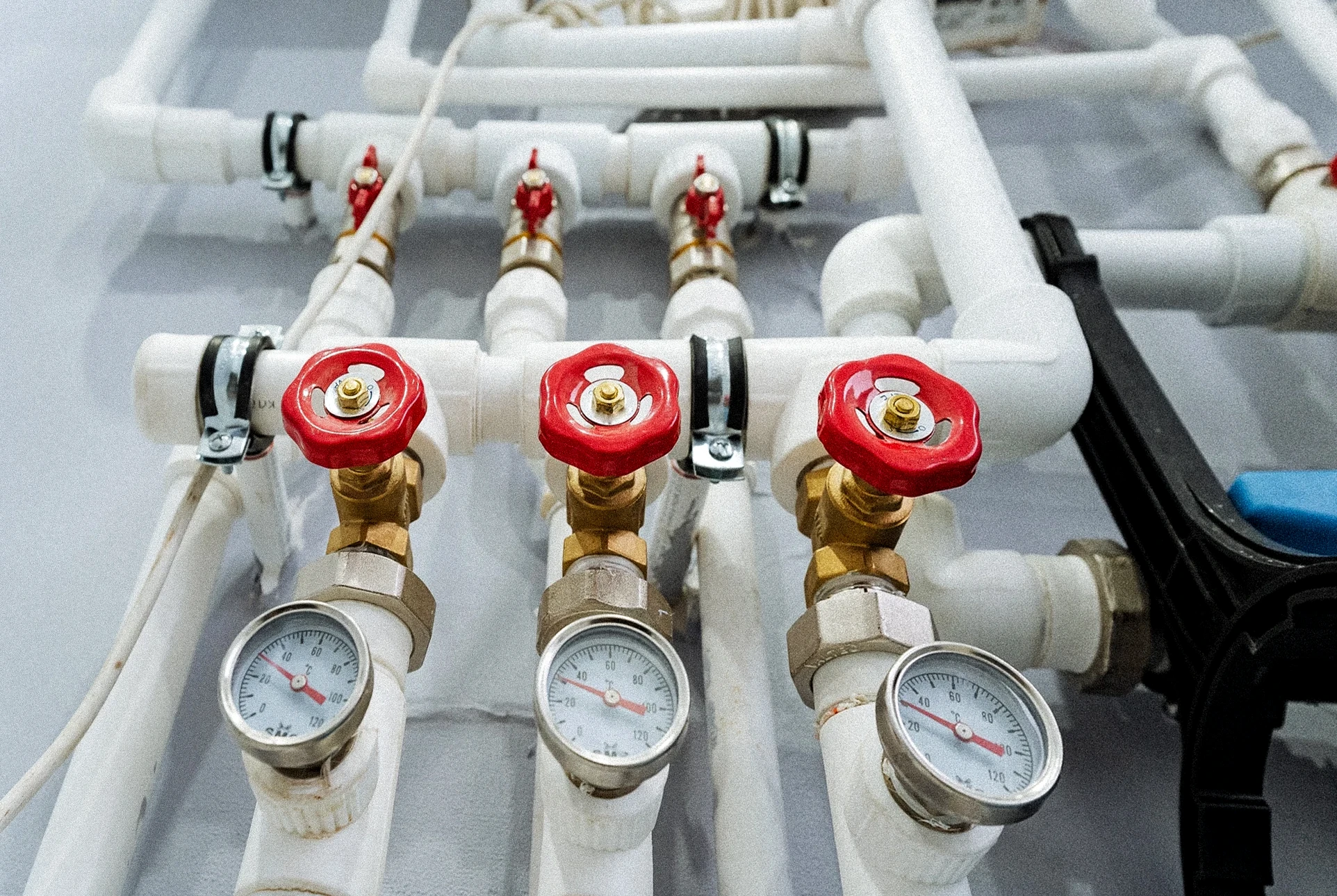 Plombier en uniforme blanc et bleu avec casquette r&eacute;pare robinetterie d'un lavabo suspendu blanc dans salle de bain carrel&eacute;e